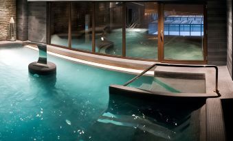 an indoor swimming pool with a hot tub , surrounded by glass walls and a wooden deck at Hotel Val de Neu G.L.