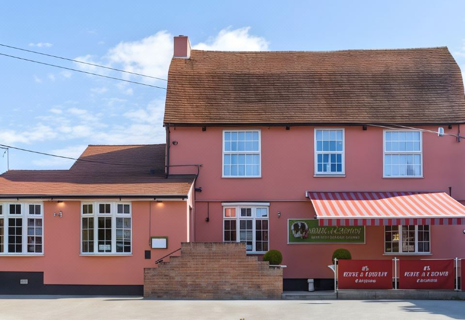 a pink building with a thatched roof and red brick trim , situated in a city street at The Rose and Crown