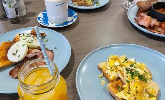 a dining table with a variety of breakfast foods , including eggs , toast , bacon , and juice at Adelong Motel