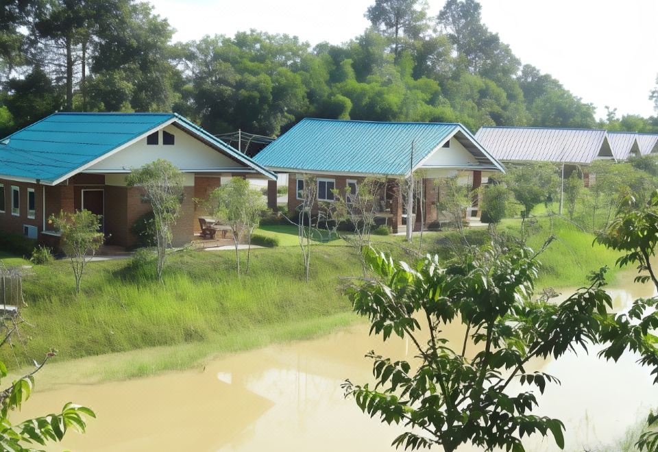 a group of small , green houses situated next to a river , surrounded by trees and grass at I Din Lake View Resort Nakhon Nayok