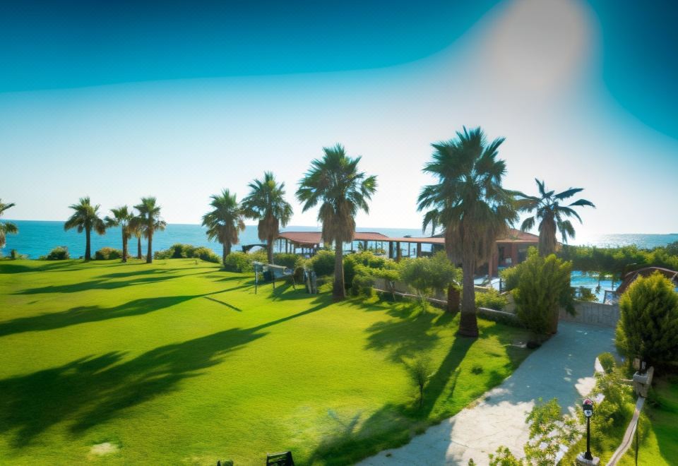 a beautiful golf course with palm trees and a body of water in the background at Poseidon Beach Hotel