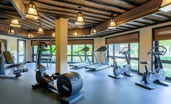 a well - equipped gym with various exercise equipment , including treadmills and stationary bikes , under a wooden ceiling at Atana Musandam Resort