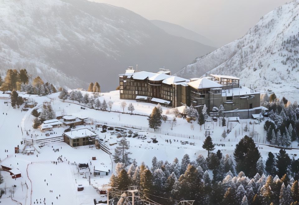 a large hotel is situated on a snowy mountain slope , with people skiing and snowboarding in the background at Pearl Continental Hotel Malam Jabba