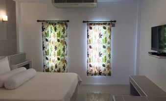 a bedroom with two window curtains , one patterned and the other floral , is shown with a bed at Saraburi Garden Resort