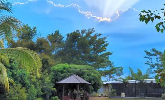 a grassy field with a gazebo in the middle , surrounded by trees and bushes , and a cloudy sky overhead at Borobudur Bed & Breakfast