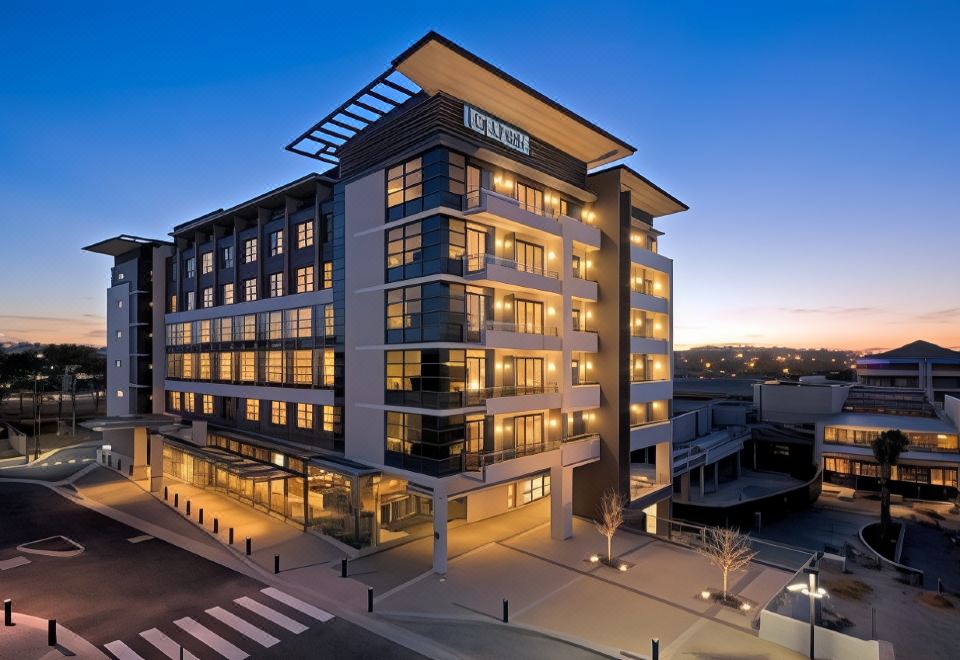 "a modern building with a large glass facade and the name "" life times "" on it is illuminated against a dark blue sky" at Rydges Campbelltown an EVT hotel