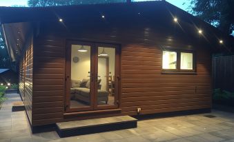 a brown wooden house with a staircase leading up to the front door , lit up at night at Shellow Lane Lodges