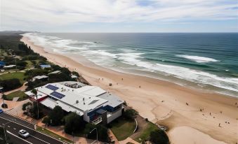 a beach scene with a building on the shore and people in the water near the beach at Coolum Caprice