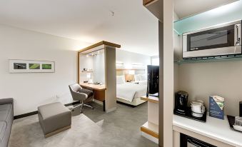 a modern hotel room with a bed , desk , chair , and kitchenette , all connected by an open door at SpringHill Suites Houston the Woodlands