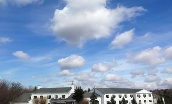 a large white building with a parking lot in front of it , under a blue sky with fluffy white clouds at The Aurora Inn Hotel and Event Center