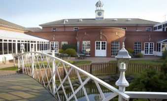 a white bridge with a clock on top is leading to a red building with a clock tower at Village Hotel Chester St David's