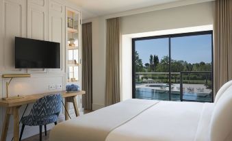 a hotel room with a large bed , a television , and a window overlooking a body of water at Hotel Camiral – The Leading Hotels of the World