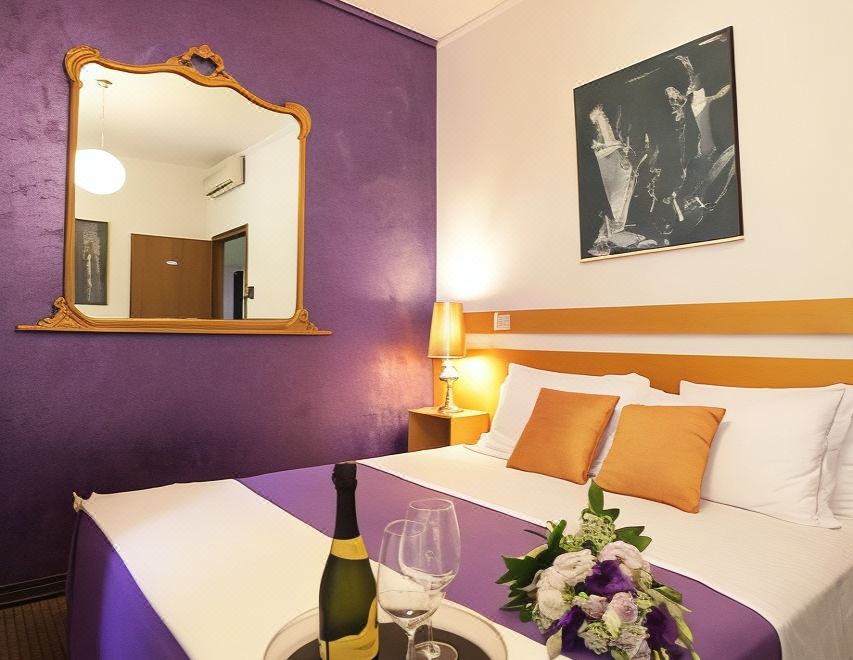 a modern hotel room with purple walls , white bedspread , gold trimmings , and a wine bottle on the bedside table at Art Hotel