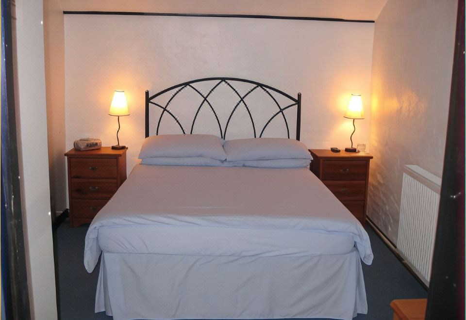 a bed with white sheets and a black metal headboard is illuminated by two lamps on either side at The Woodlands