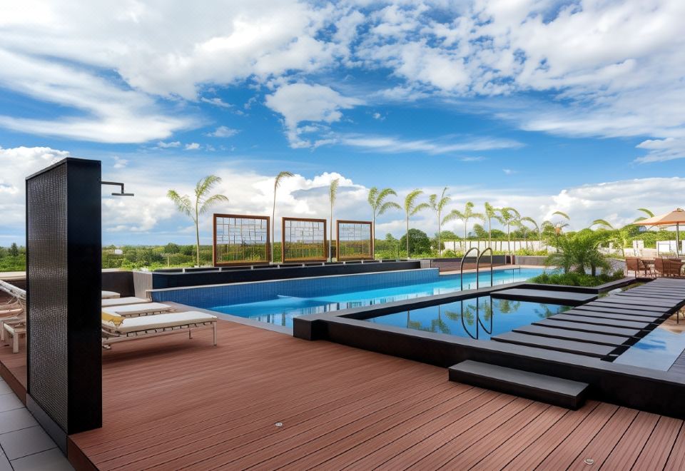 a rooftop pool surrounded by wooden decking , with lounge chairs and umbrellas placed around the pool area at Neelkanth Sarovar Premiere