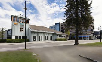 a large building with a blue roof and white walls is situated next to a tree on the street at Quality Hotel Grand Kongsberg