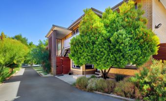 a brick building with a red door , surrounded by green trees and a parking lot at Lake Wendouree Luxury Apartments