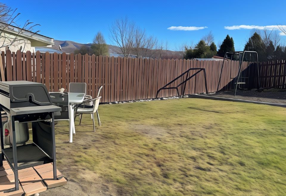 a backyard with a wooden fence , a barbecue grill , and a black metal fence , under a clear blue sky at Pinewood Motels