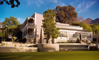 a large white building surrounded by a lush green lawn , with trees in the background at Schoone Oordt Country House