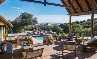a luxurious outdoor living area with wooden furniture , umbrellas , and a pool under a thatched roof at Bukela Game Lodge - Amakhala Game Reserve