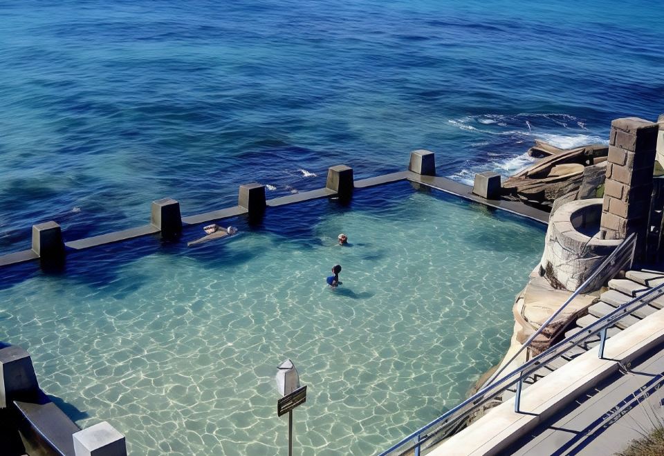 a large swimming pool with a dock and people in it , overlooking the ocean at Coogee Sands Hotel & Apartments