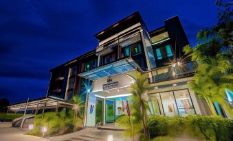 a modern building with a blue sign and palm trees in front of it at night at The Living Hotel SamutPrakan