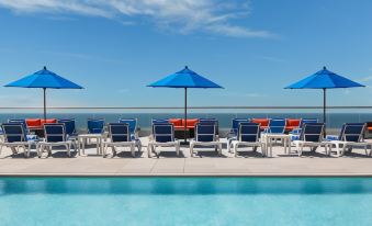 a large pool surrounded by lounge chairs and umbrellas , with a view of the ocean in the background at Allegria Hotel