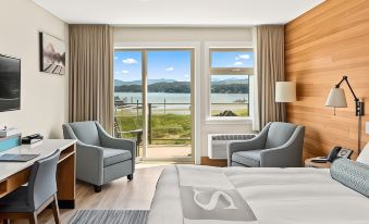 a hotel room with a bed , chairs , and a large window overlooking a body of water at Sproat Lake Landing Resort