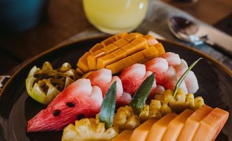 a plate of food with various fruits and vegetables , a glass of orange juice in the background at Karpaha Sands