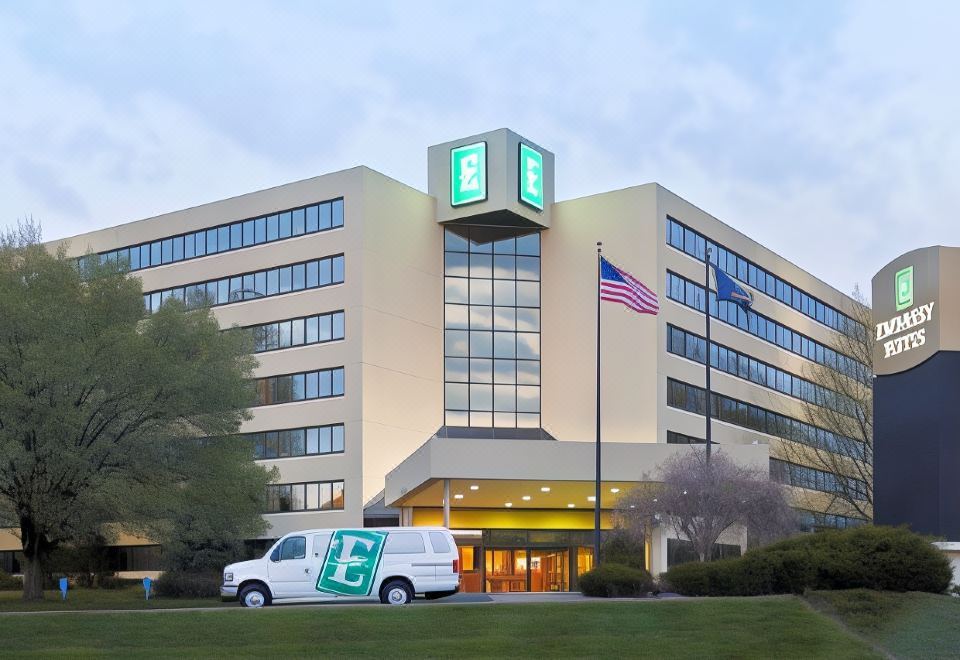 a white van is parked in front of a building with an american flag and the letter e on it at Embassy Suites by Hilton Kansas City Overland Park