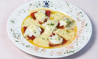 a white plate filled with sliced mozzarella and tomatoes , drizzled with a yellow sauce , sitting on a dining table at Hotel Castillo
