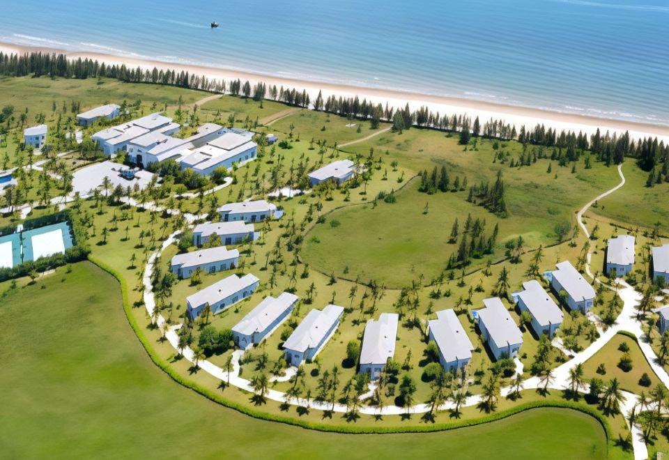 a bird 's eye view of a resort with multiple buildings , green spaces , and a beach in the background at Melia Vinpearl Cua Sot Beach Resort