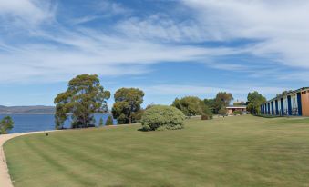 a large green field with trees and a house in the background , under a blue sky with clouds at Riverfront Motel & Villas
