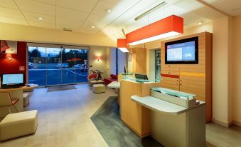 a modern office with a reception area , where a man is sitting on a red chair at Ibis Clermont-Ferrand Sud Carrefour Herbet