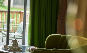 a living room with a green couch , wooden floor , and a view of a balcony through the window at Les Sources de Cheverny