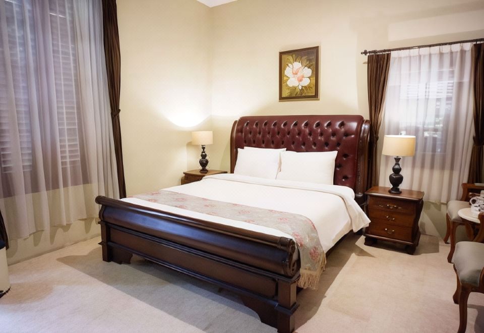 a large bed with a brown headboard is situated in a bedroom with two lamps and a painting on the wall at Griya Gendhis Saraswati