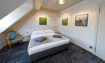 a cozy bedroom with a bed , two chairs , and a painting on the wall , under a sloping ceiling at Fleur de LIS