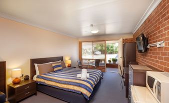 a hotel room with a king - sized bed , a television , and a door leading to a balcony at Lake Macquarie Motor Inn