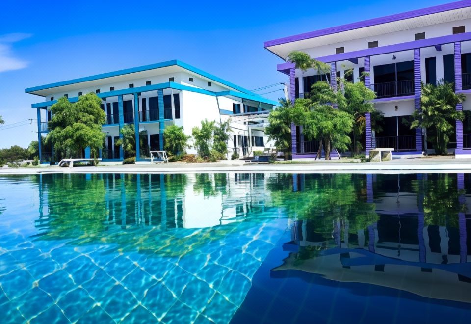 a large swimming pool with a blue and white building in the background , surrounded by lush greenery at Menam Resort