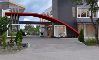 a red archway entrance to a modern building with a car parked outside , under a cloudy sky at Hotel Kings Kudus