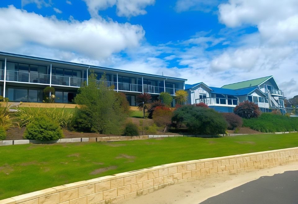 a modern building with a stone wall and green grass , set against a blue sky with white clouds at Swansea Motor Inn Tasmania