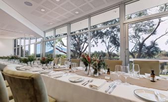 a large dining room with a long table set for a formal dinner , surrounded by windows overlooking trees at Royal Mail Hotel