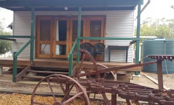 a small wooden house with a porch and a green bench , surrounded by rusted wheels at Stone Hut Cottage