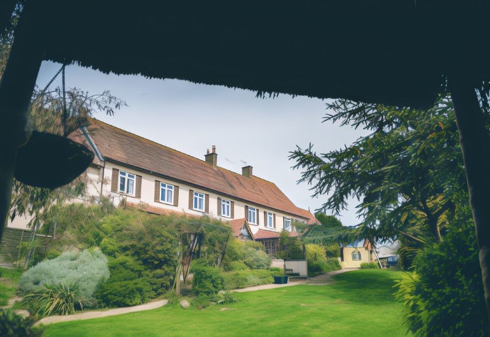 a large , two - story house with a green lawn and trees in the foreground , under a cloudy sky at The Grange Hotel Brent Knoll