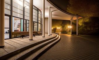 a modern building with a curved walkway and large columns , lit by lamps in the evening at FlyOn Hotel & Conference Center