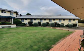 a building with a red roof and white trim is surrounded by trees , bushes , and a grassy area at The Aston Motel Tamworth