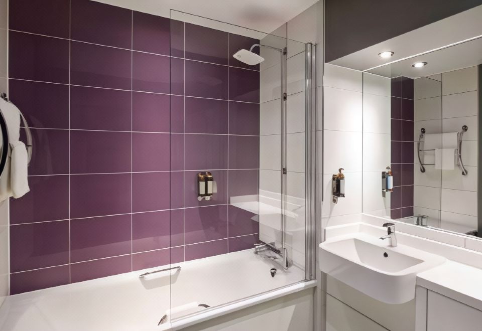 a modern bathroom with purple tiled walls , a white bathtub , and a clear glass shower enclosure at Premier Inn Bagshot