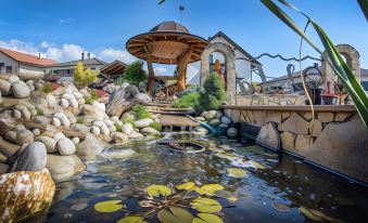 a pond with rocks , a wooden gazebo , and a walkway leading to a stone building at VeLa