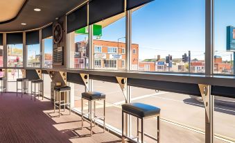 a bar with three stools , one on the left and two on the right , along with a view of the city outside at The Lighthouse Hotel