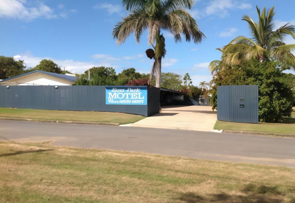 a motel with a large blue sign on the side , surrounded by trees and grass at Emu Park Motel